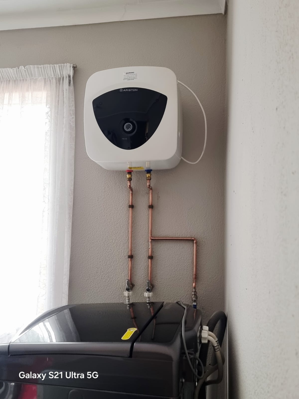 Compact electric geyser installed above a washing machine